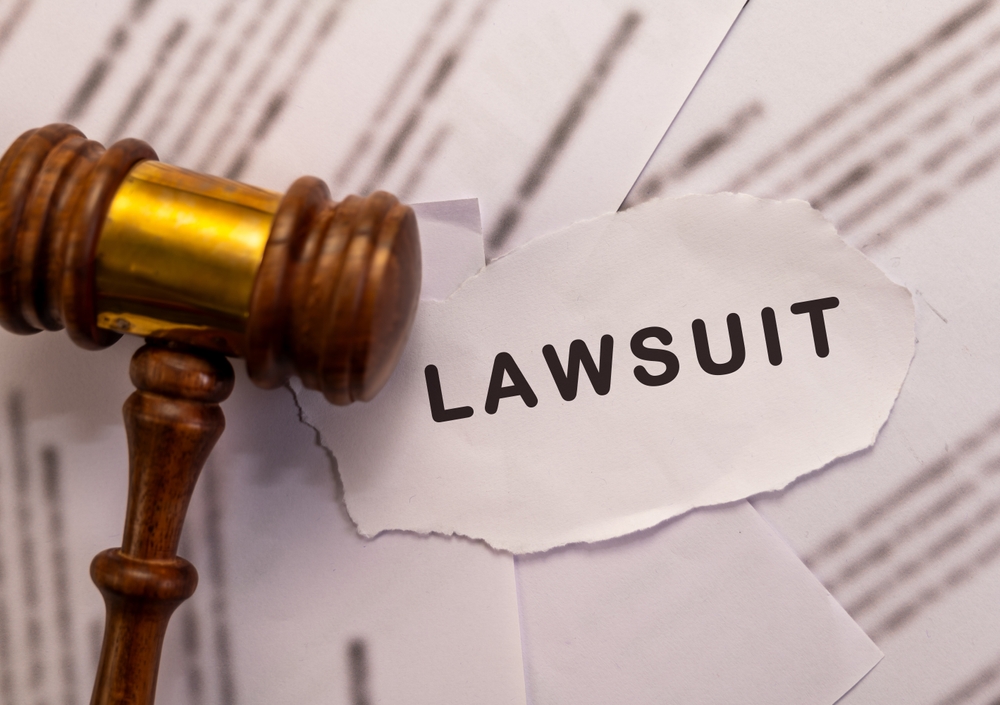 A wooden gavel rests on papers, one of which has "LAWSUIT" printed in bold—suggesting the serious step a creditor might take and raising questions like how much does it cost a creditor to sue you.