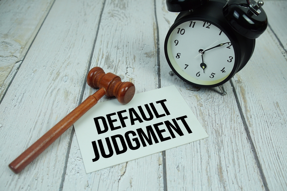 Default Judgment text on paper card with alarm clock and wooden judge gavel top view on wooden background