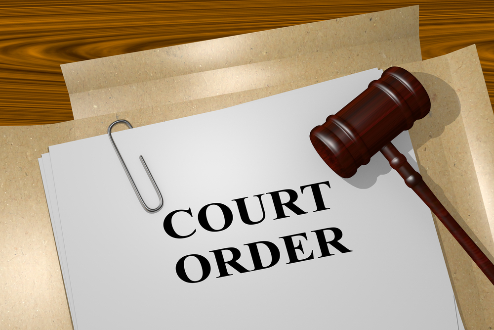 A judge's gavel rests on a stack of papers labeled "Court Order," referencing custody issues all held together with a paperclip on a wooden desk.