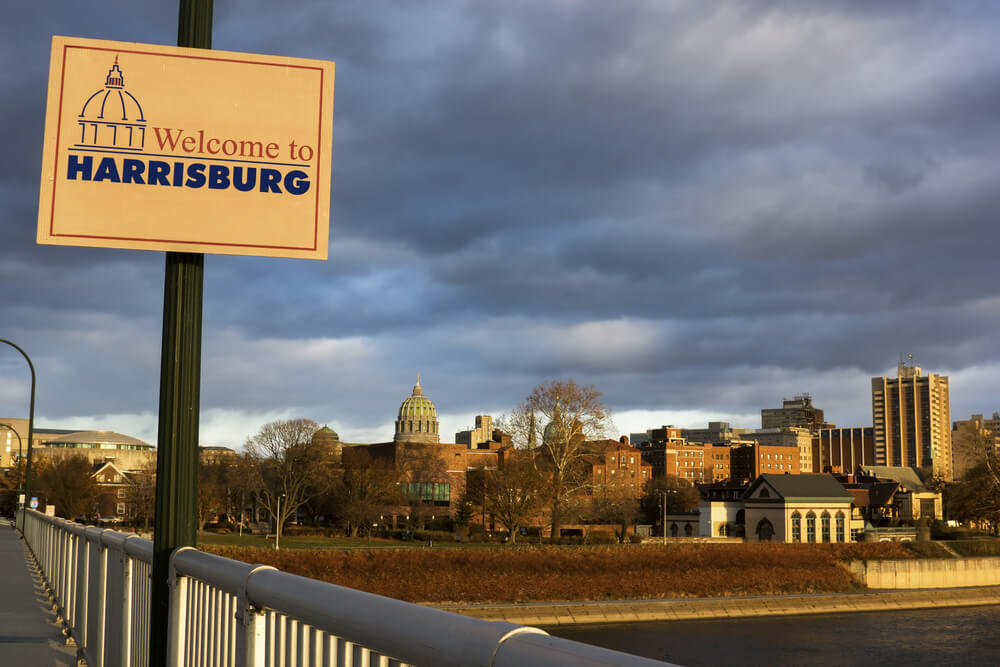 A welcome to  Harrisburg, PA sign with the city in the background 
