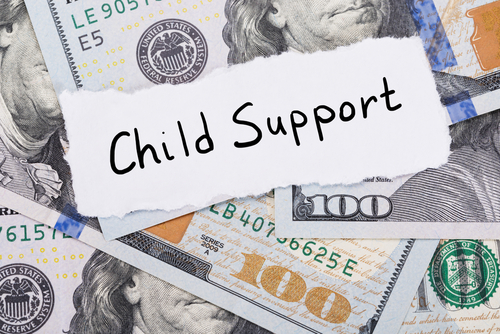 Child Support" written on torn paper over a backdrop of U.S. hundred-dollar bills, subtly questions fairness, especially if the custodial parent makes more money.