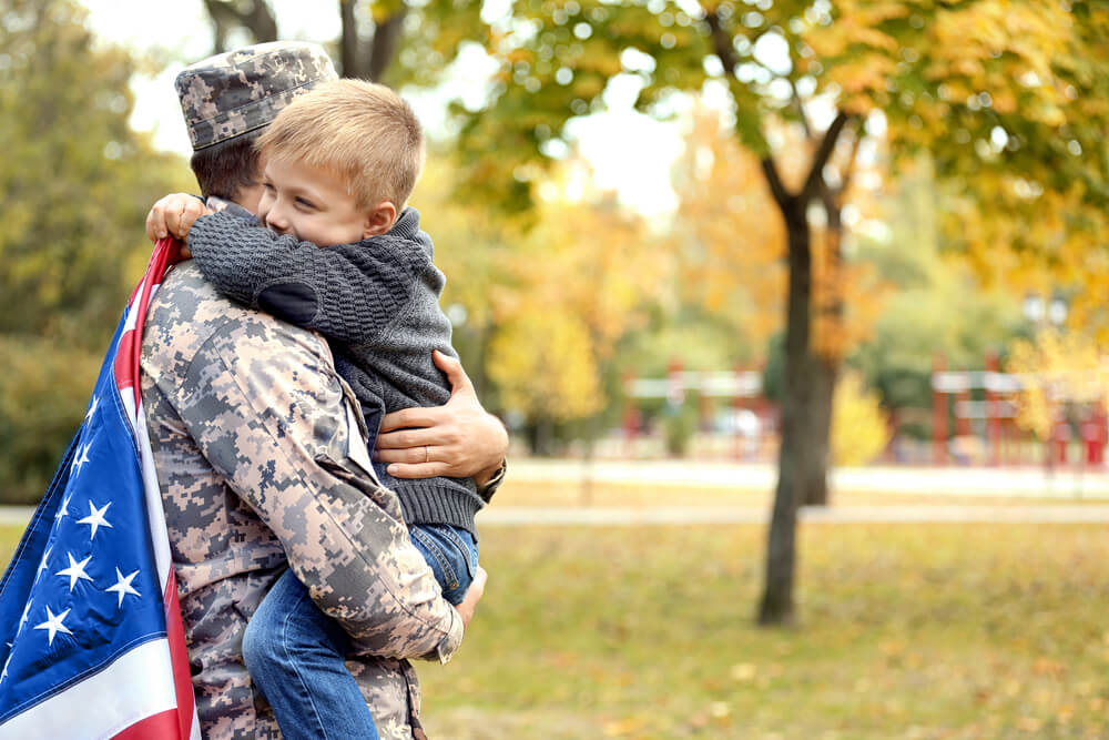 A solider lifting a little boy and the boy is wrapped around the solider and holding the United States flag 