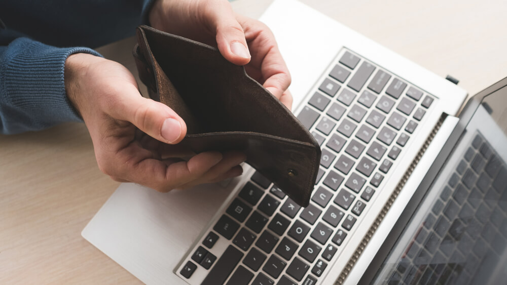 A close up of a man opening his wallet over his laptop and there is not money inside