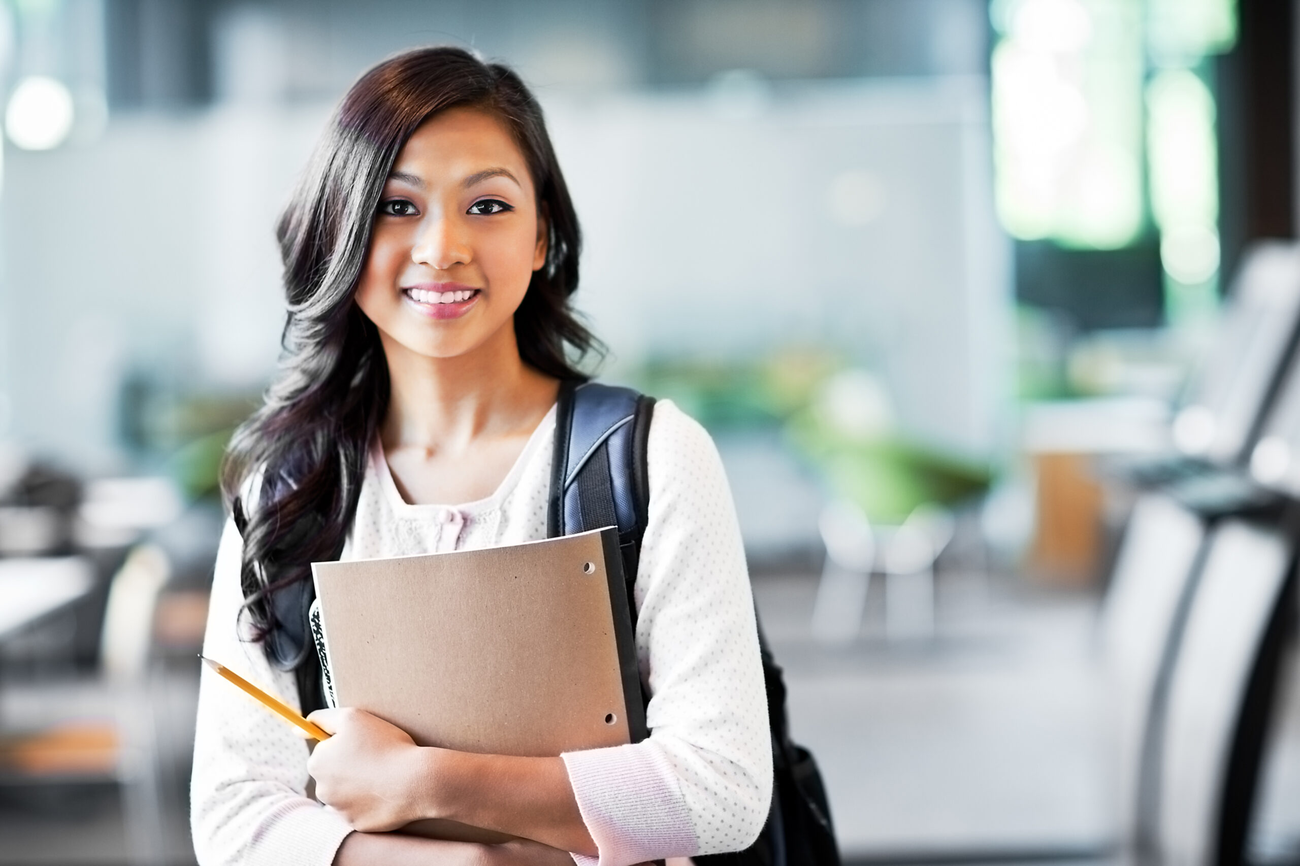 Young woman student with a backpack and holding notebooks and a pencil