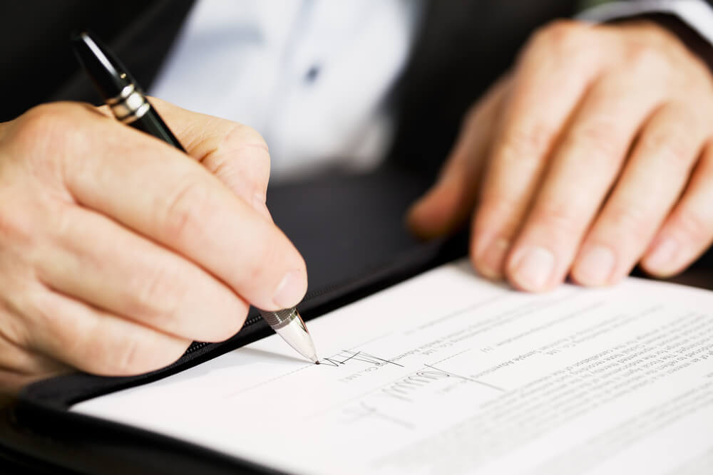 A man signing a document on a dark surface 