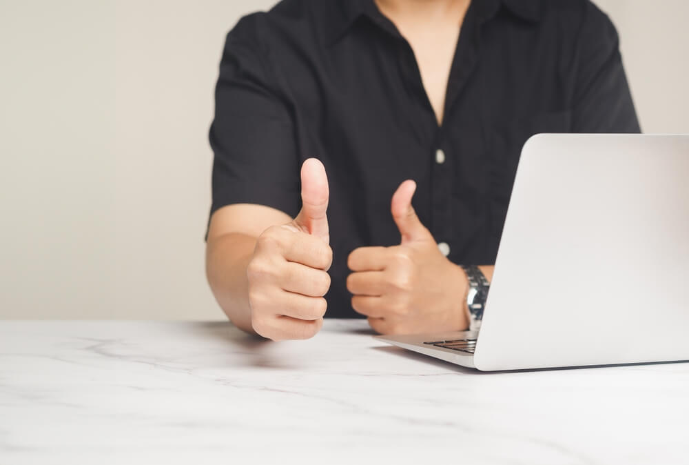 Someone sitting at their desk with the laptop open and they have both thumbs up 