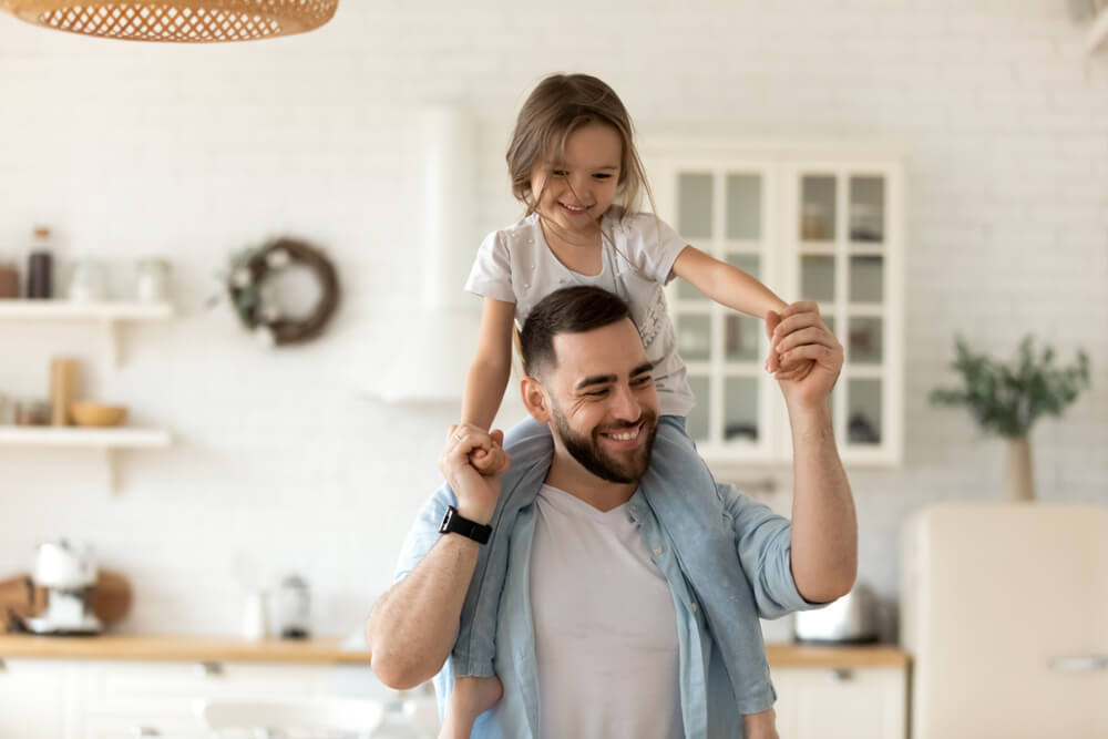 A dad holding his daughter on his shoulders and the two are smiling and having fun 