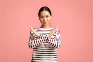Women standing against a pink wall holding her arms up in the shape of an X
