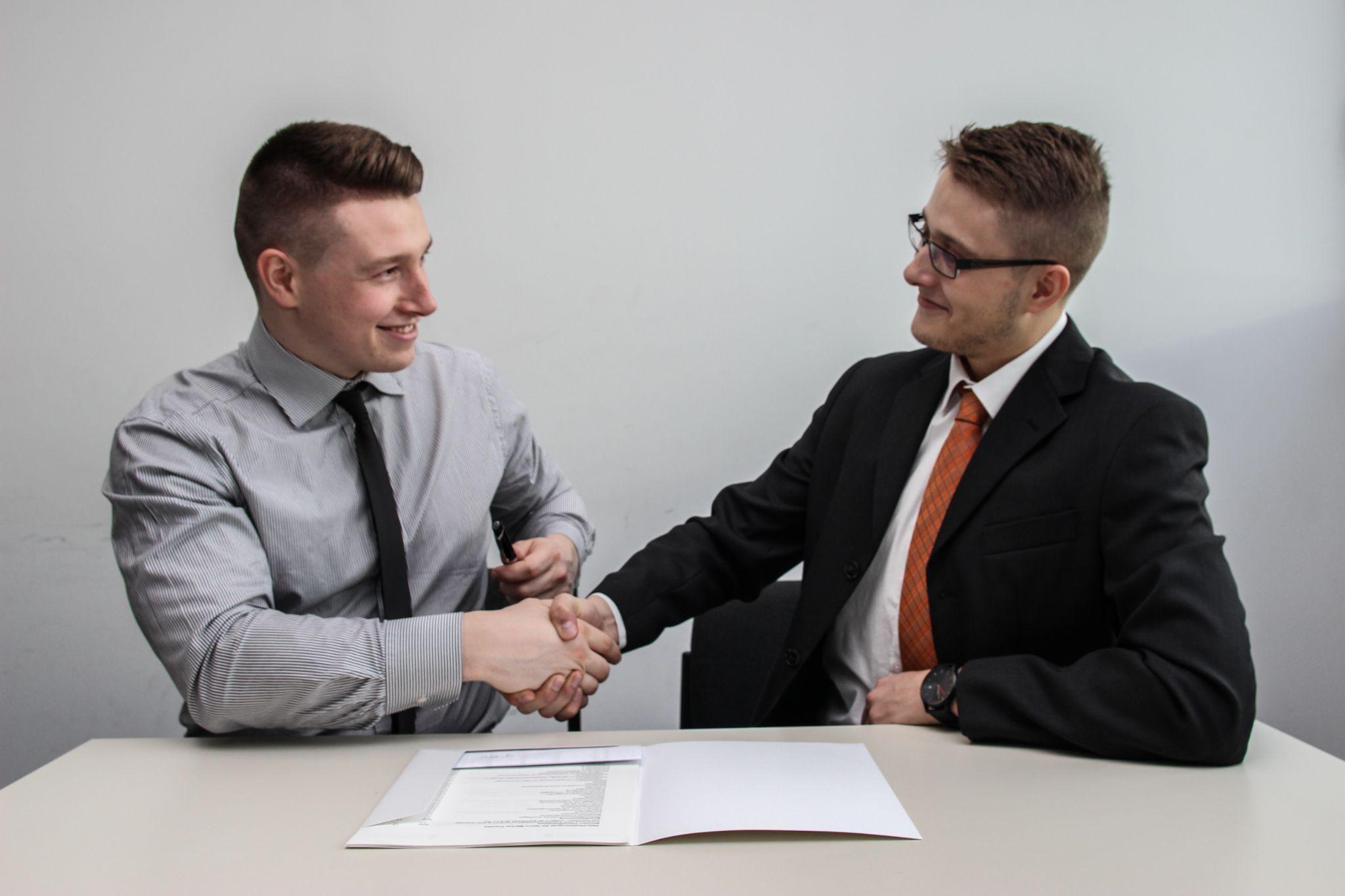 Two men are shaking hands at a desk in an office discussing legal issues.