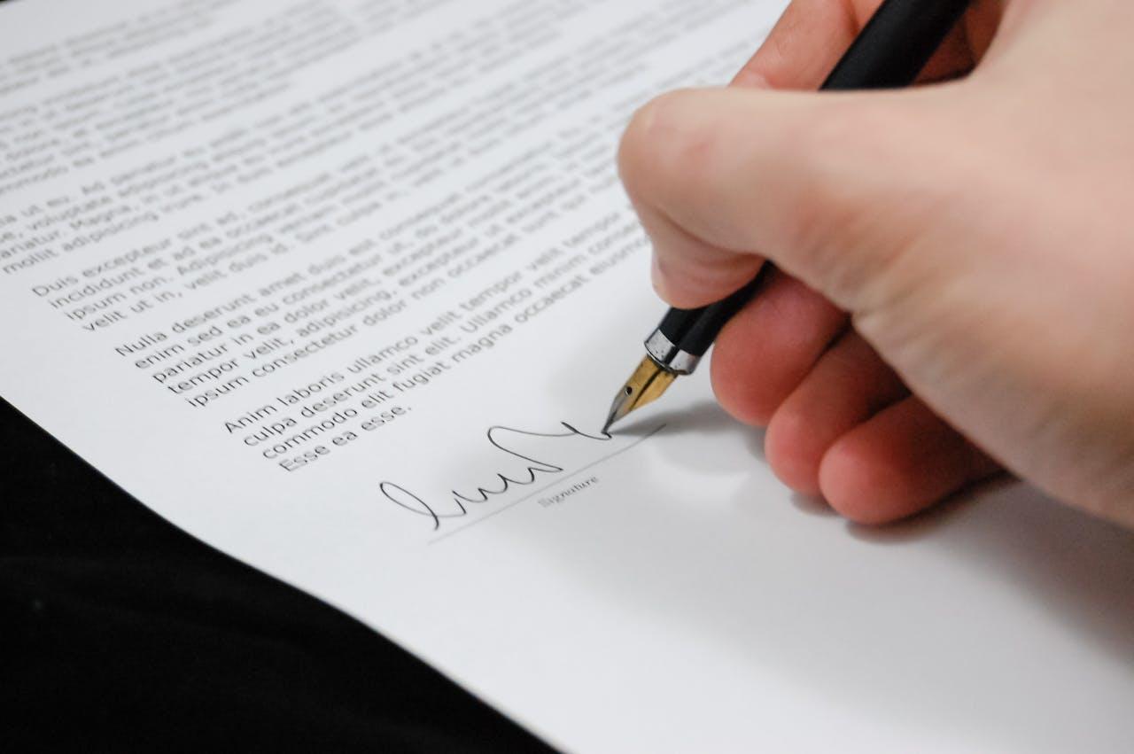 A person signing a document with a pen
