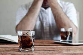 A man sitting at a table with a glass of cola, contemplating his situation.