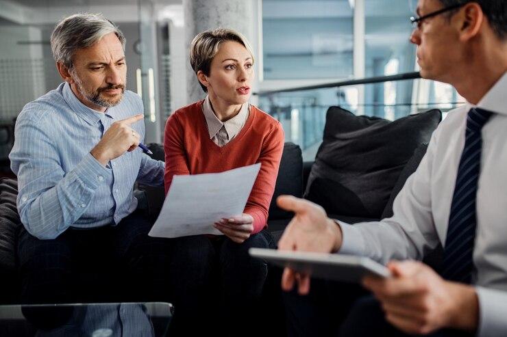 Three professionals in a discussion, with paperwork and a digital tablet.