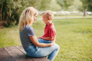 A woman and a young boy sitting face-to-face on a park bench, engaging in a conversation about the benefits of primary physical custody.