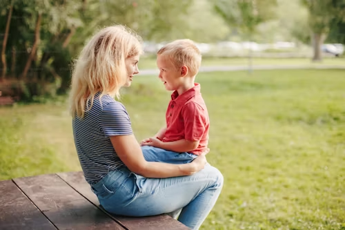 A woman and a young boy sitting face-to-face on a park bench, engaging in a conversation 