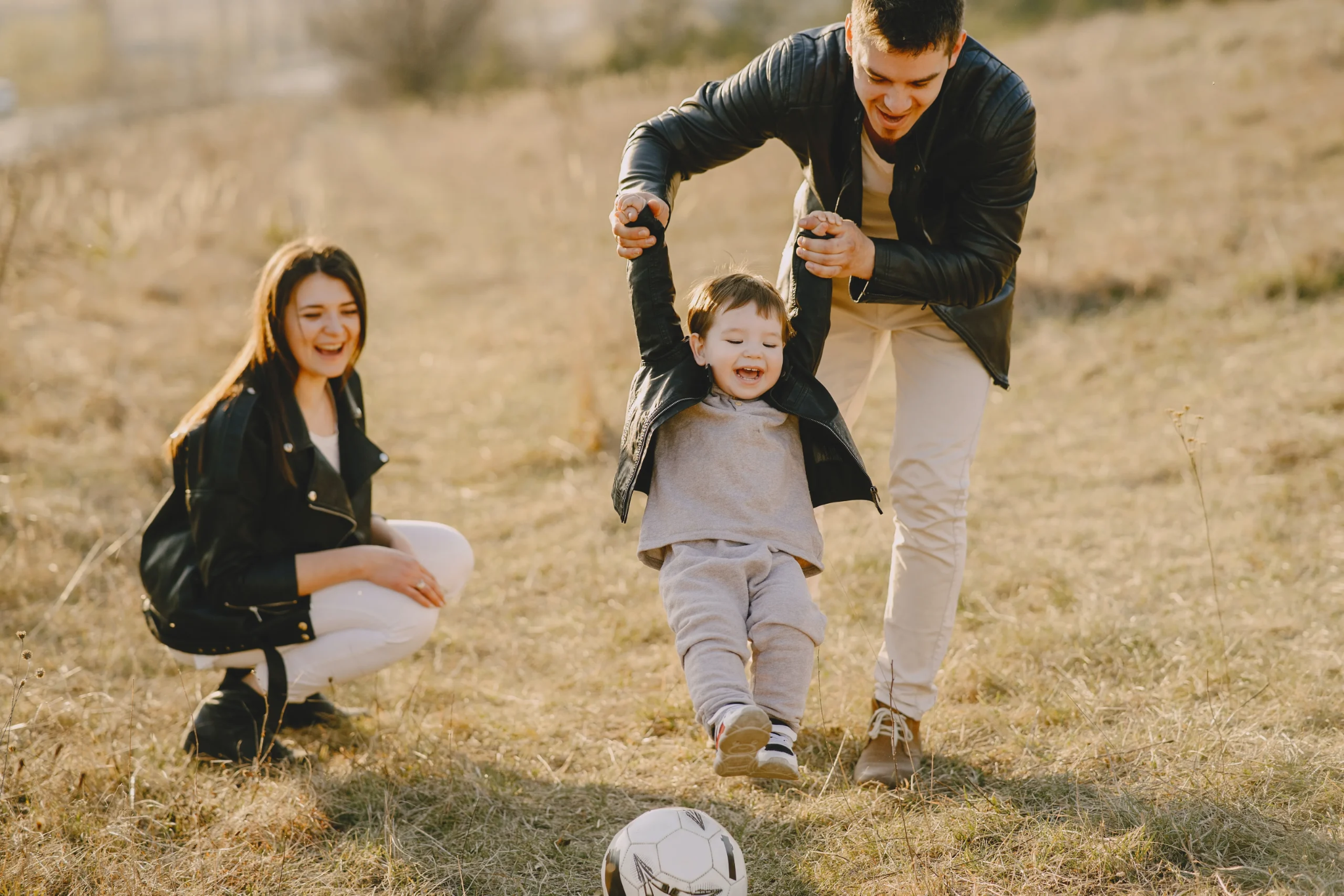 Family enjoying outdoor time together with a focus on a child taking first steps toward a soccer ball.