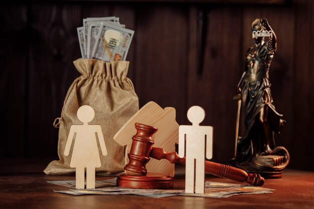 Wooden figures representing two people, a gavel, and money on a table, symbolizing legal judgment and financial dealings