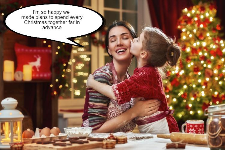 A child kissing a smiling woman on the cheek in a festive kitchen with a Christmas tree in the background.