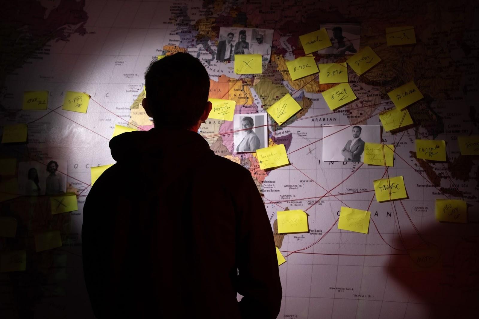 A person standing in front of a world map with various notes and pictures attached