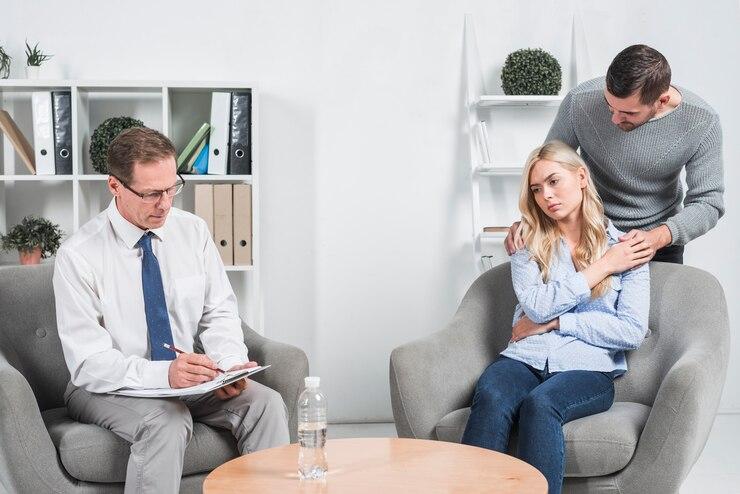 A couple in therapy session, with a counselor taking notes.
