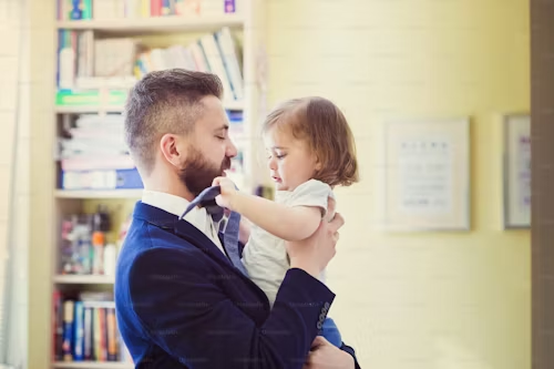 A man in a suit, holding a toddler who is touching his face.