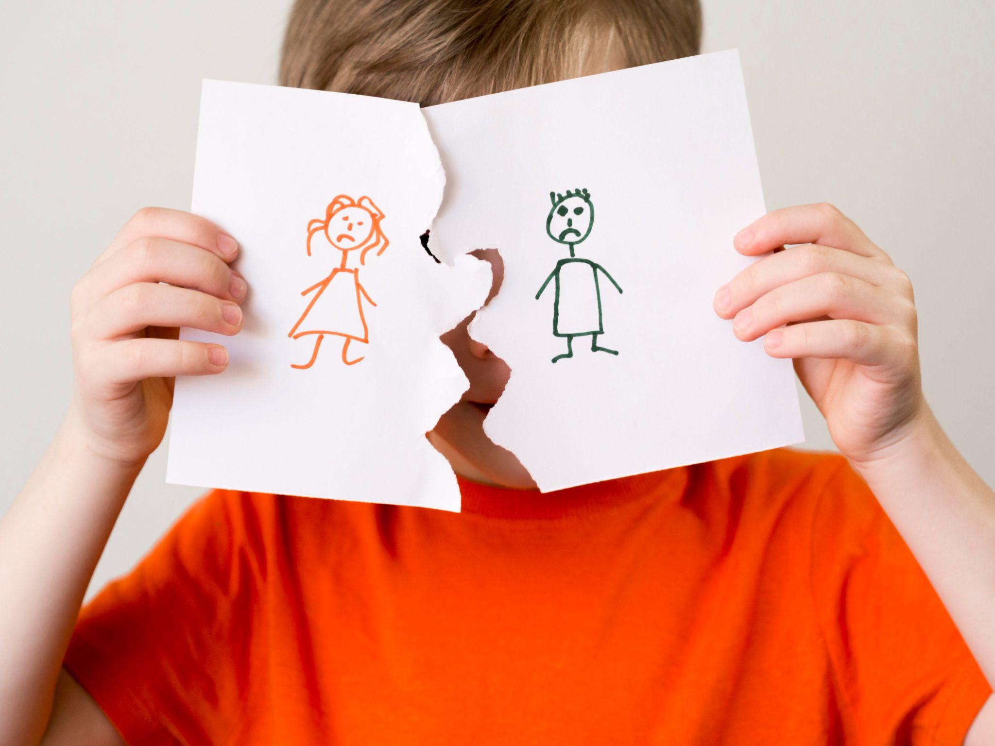 Child holding a torn piece of paper with a drawing of a girl on one half and a boy on the other, symbolizing a split or separation.