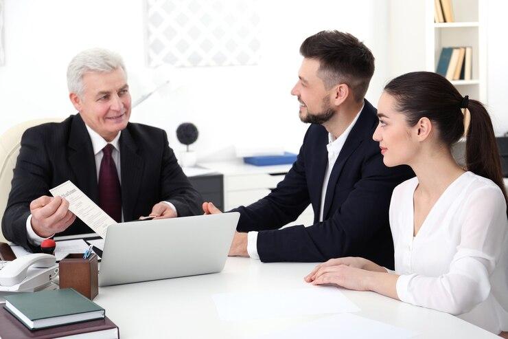 Three professionals in a meeting, with an older man as he hands a document to a younger man and woman who are looking at it attentively.