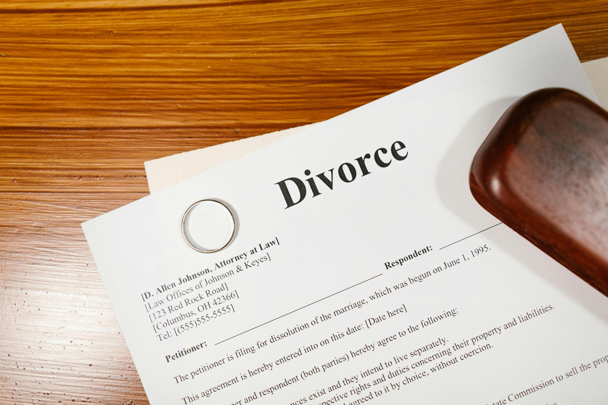 A close-up of a divorce document from J.D. Allen Johnson Attorneys at Law on a wooden table. A wedding ring and a wooden gavel are placed beside it.