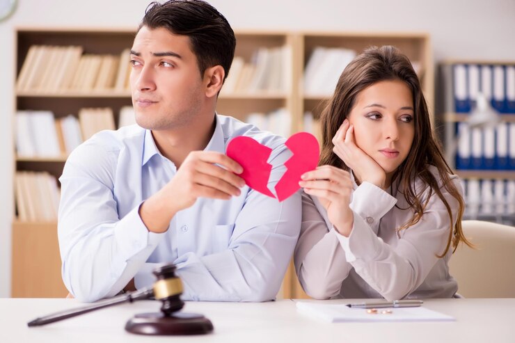 Two parents seated apart at a table holding halves of a paper heart; gavel and documents on the table.