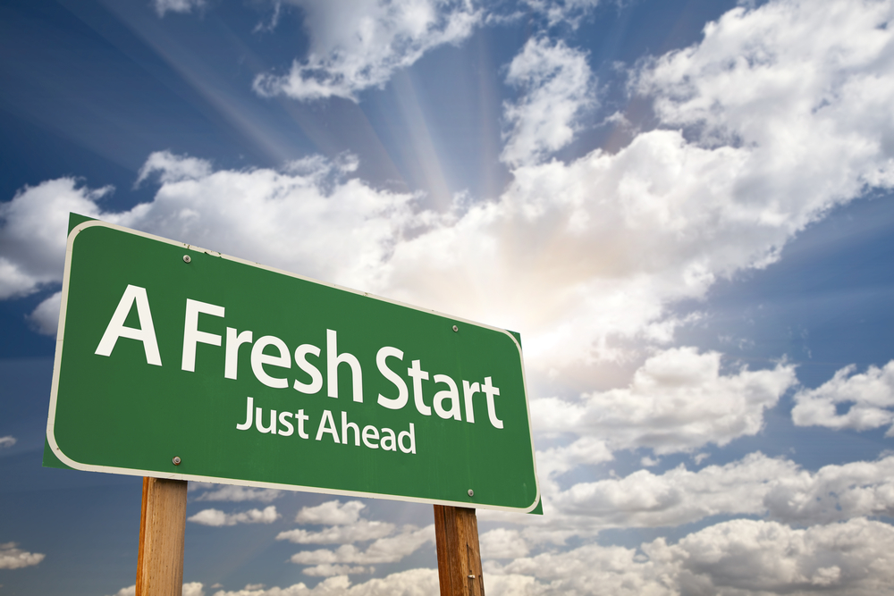 A green road sign reads "A Fresh Start Just Ahead" against a backdrop of a cloudy sky with rays of sunlight breaking through.