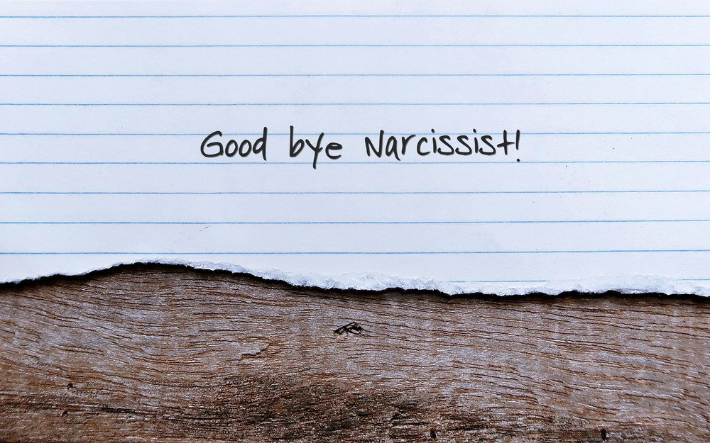 Lined paper with "Goodbye Narcissist!" scrawled across it lies on a wooden surface. A tiny ant meanders below, seemingly indifferent to the seismic shifts that accompany such personal journeys.