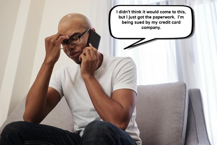 A person in a white t-shirt sits on a couch, holding a phone to their ear, looking distressed. 