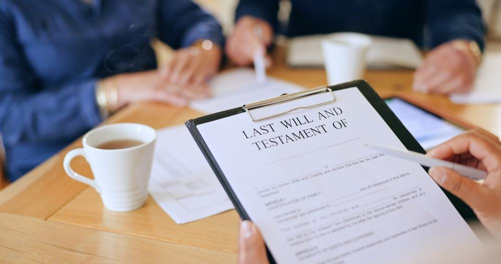A person holds a clipboard with a "Last Will and Testament" as two others sit at a table with coffee and books, discussing how to protect your estate in Texas.